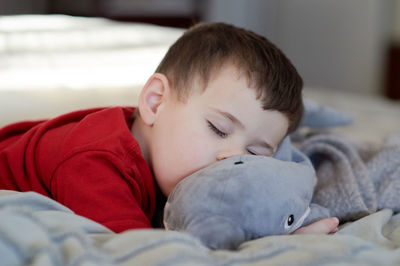 Young boy taking a nap on the bed using his plush toy as a pillow