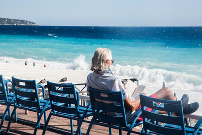 Rear view of woman sitting on chair at beach