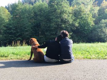 Rear view of couple sitting on grass against trees