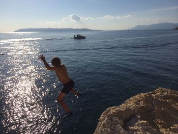 Boy jumping into sea against sky