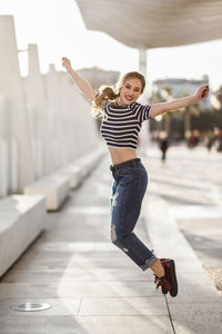 Full length of beautiful young woman jumping on footpath in city