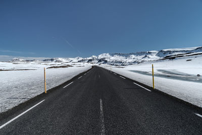 Road on snow covered landscape against clear sky