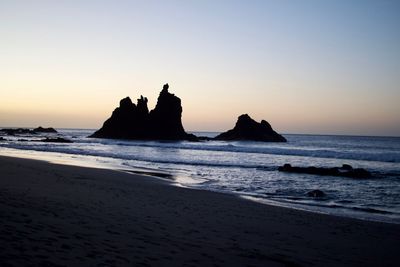 Silhouette rocks on beach against sky during sunset