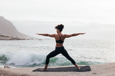 Rear view of woman exercising at beach against sky