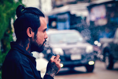 Side view of young man smoking cigarette while standing on road