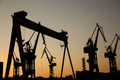 Silhouette cranes at construction site against sky during sunset