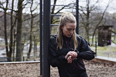 Female athlete checking smart watch while leaning on monkey bars in forest