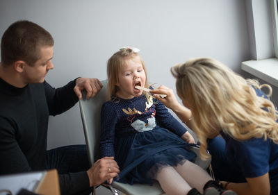 Female doctor examining girl sitting on chair with father in hospital