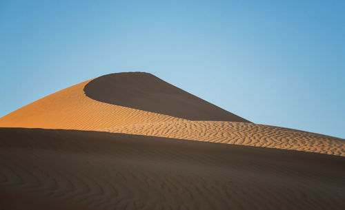 Low angle view of sand dunes against clear blue sky