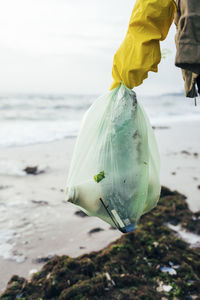 Woman holding garbage bag against sea