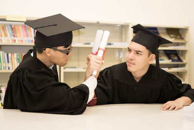 Students in graduation gowns sitting at table in library