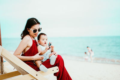 Mother and son relaxing at beach against sky