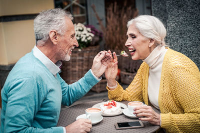 Smiling senior man feeding wife while sitting at cafe