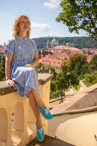 Full length of woman sitting on wall against townscape