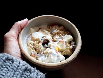 Cropped hand holding bowl with food over black background