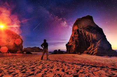 Rear view of man standing on rock against sky