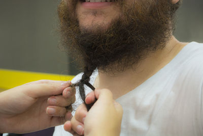 Cropped hands of person tying beard of man