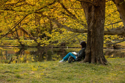 Attractive young woman reading book while sitting on grass in green public park. springtime outdoors