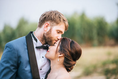 Man kissing woman on forehead against sky