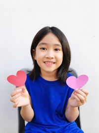 Portrait of young woman holding heart shape against white background