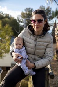 Portrait of mother carrying daughter while sitting against trees