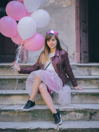 Portrait of young woman holding pink balloons while sitting on steps