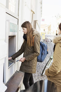 Side view of young woman using cash machine