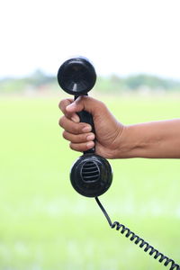 Close-up of hand holding telephone against sky