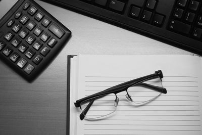 Close-up high angle view of laptop with eyeglasses and book by calculator on table