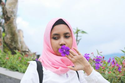 Young woman wearing hijab holding purple flower while looking away