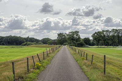 Scenic view of straight road through fields against sky