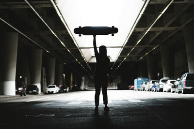 Silhouette woman holding skateboard while standing in parking lot