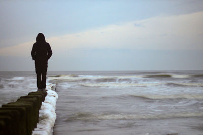 Rear view of man standing on groyne in sea against sky