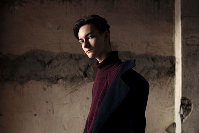 Portrait of young man standing by weathered wall