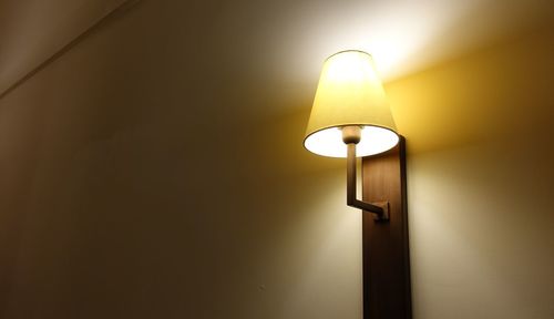 Close-up of illuminated light bulb against wall at home