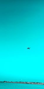 Airplane flying over sea against clear blue sky