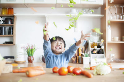 Happy boy tossing vegetables in kitchen at home