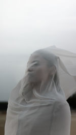 Young woman covering face while standing against sky