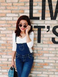 Portrait of young woman wearing sunglasses standing against brick wall