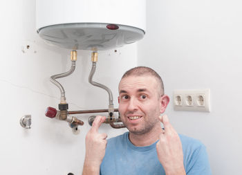 Portrait of mature man with fingers crossed standing against wall in bathroom