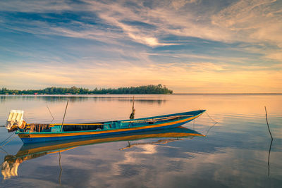 Boat moored in lake against sky during sunset