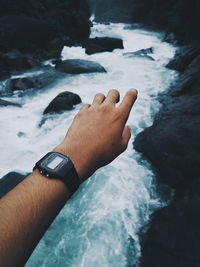 Cropped hand of man wearing wristwatch over stream