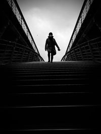 Full length of woman walking on footbridge against sky