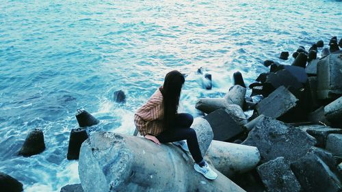 High angle view of woman sitting on tetrapod in sea