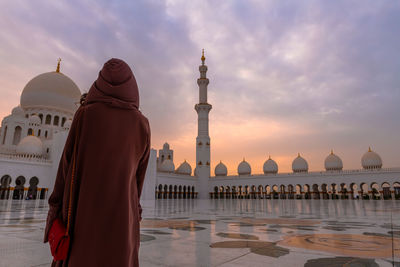 Rear view of woman standing at historic mosque against cloudy sky