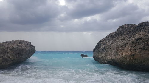 Scenic view of sea and rocks against cloudy sky