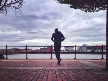 Woman standing by railing against cloudy sky