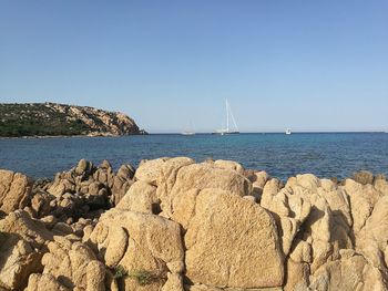 Sailboats on rocks by sea against clear sky
