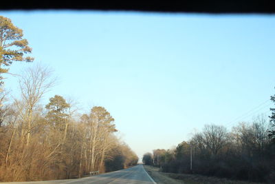 Road amidst trees against clear blue sky