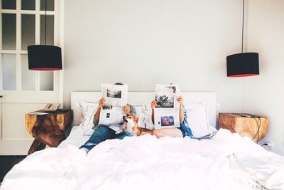 Couple reading newspaper while sitting on bed at home